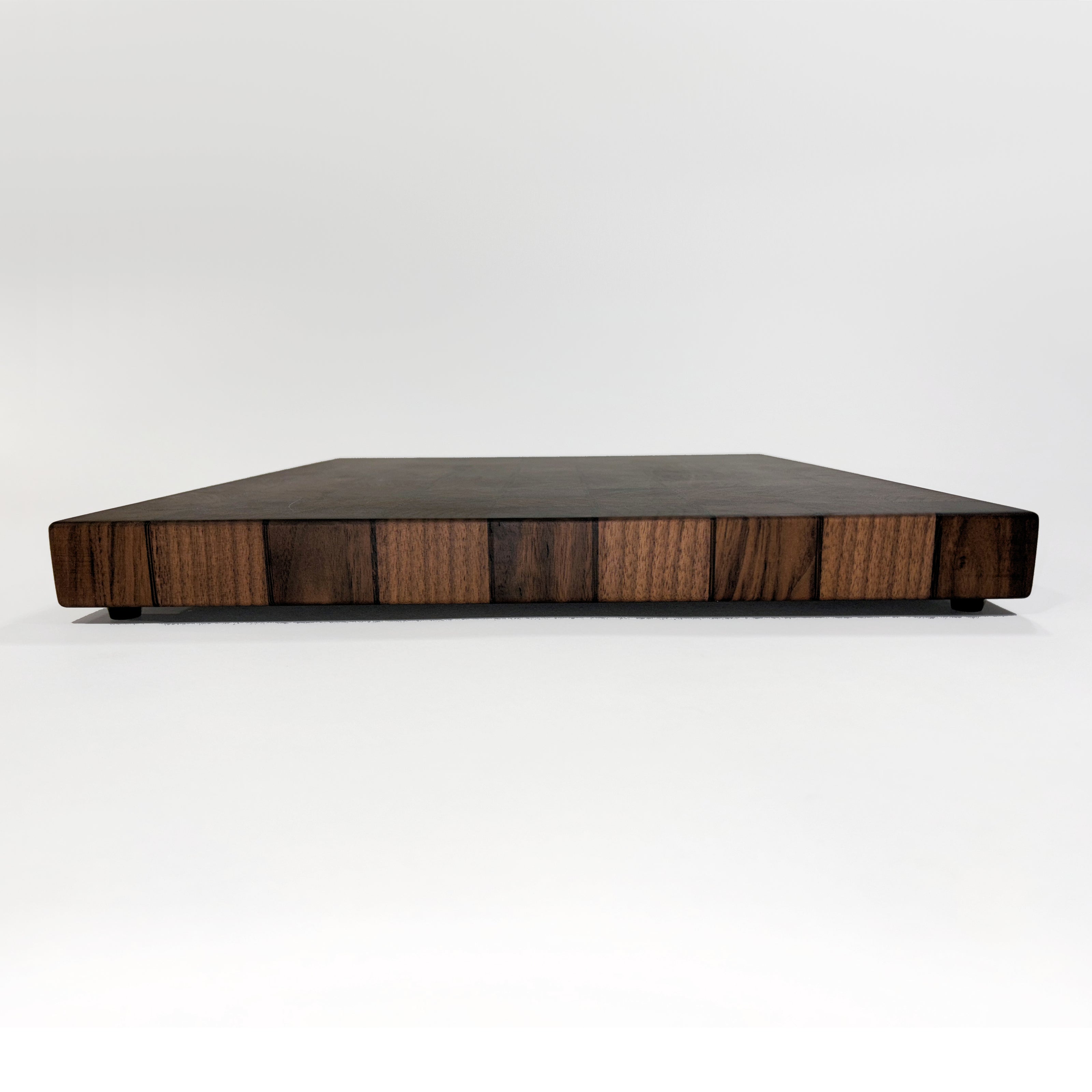 A rectangular wooden cutting board with a dark top surface and a striped wood-grain patterned side, photographed on a seamless white studio background.